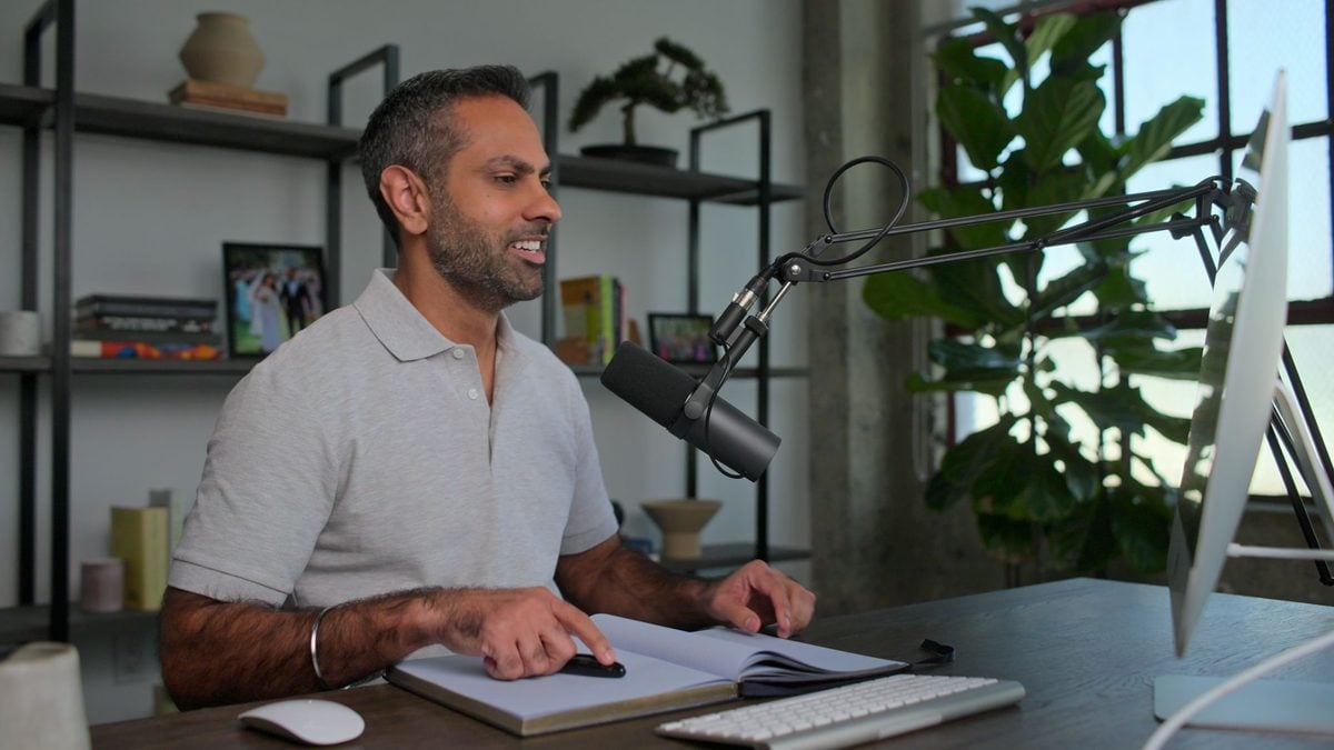 Ramit at his desk with a notebook open, talking into a microphone